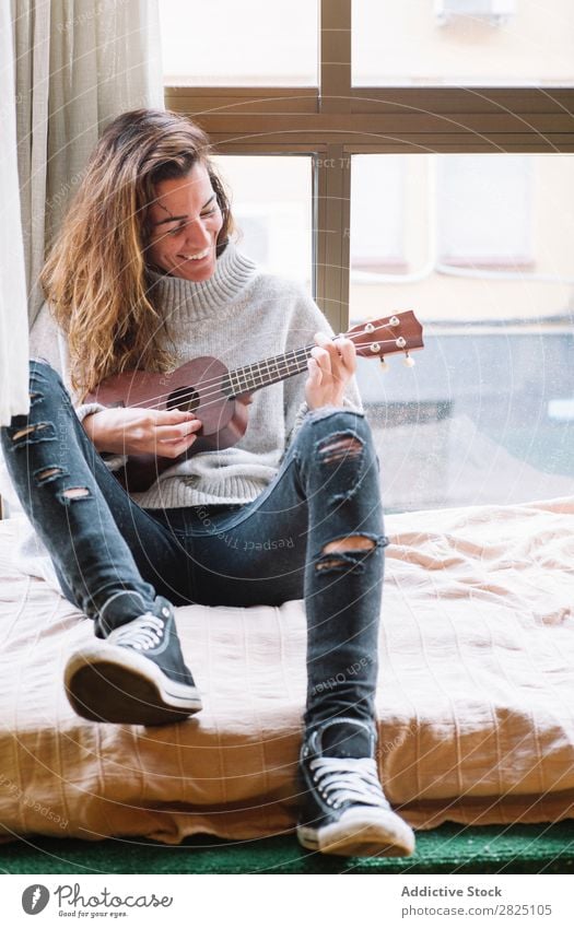 Fröhliche Frau beim Ukulelele spielen heimwärts Erholung Spielen Lifestyle Musiker heiter Lächeln schön Raum Mensch lässig Erwachsene Haus Beautyfotografie