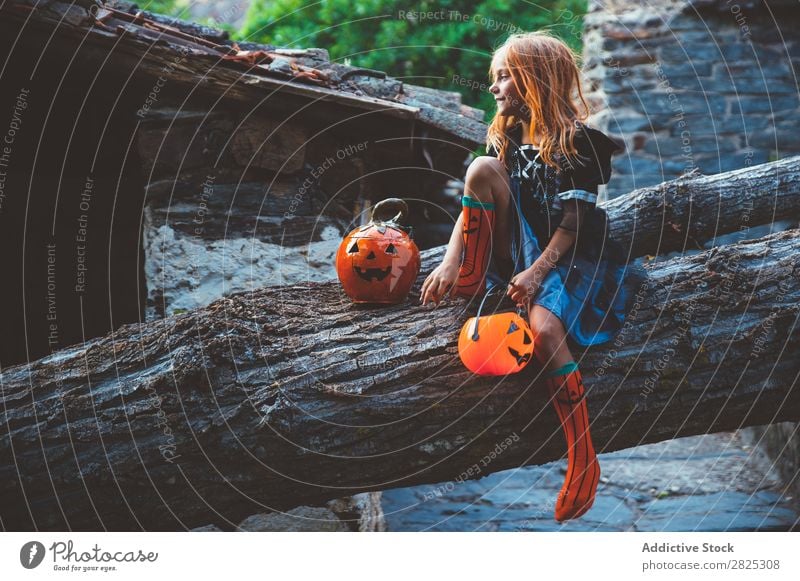 Fröhliches Kind im Kostüm, das auf einem Baum posiert. Mädchen Halloween Körperhaltung Feste & Feiern Tradition Zauberei u. Magie Ausdruck Süßwaren Bekleidung