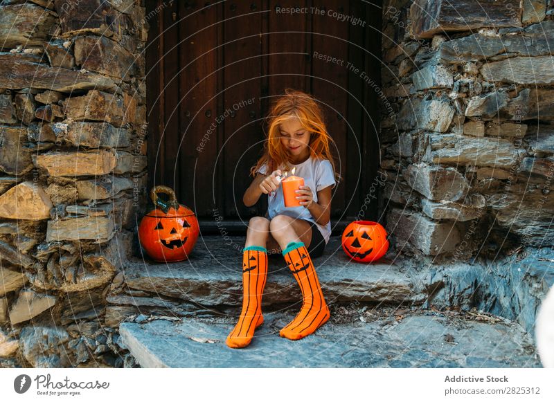 Charmantes Mädchen zündet Kerze auf der Veranda an. Halloween Kürbis Beleuchtung Gast Tradition Dekor Design Ferien & Urlaub & Reisen Herbst Festspiele Kind