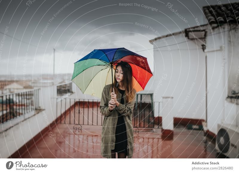 Mädchen mit Regenschirm gegen bewölkten Himmel. Frau stehen Halt mehrfarbig Regenbogen grau Wolken Wetter Außenaufnahme Dach Gebäude horizontal Porträt