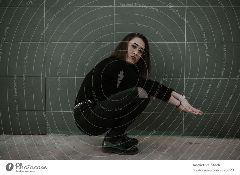 Frau, die auf Hunkern sitzt. hübsch Jugendliche schön sitzen Brillenträger Coolness Blick in die Kamera Wand grau brünett attraktiv Mensch Beautyfotografie