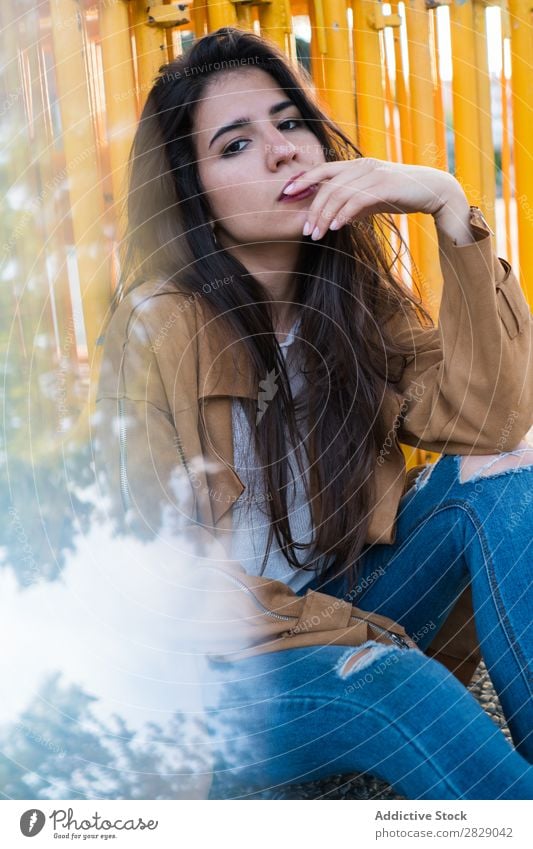 Junge und hübsche Brünette, die draußen sitzt und nachdenklich aussieht. Frau Stil besinnlich Außenaufnahme Stadt modern trendy elegant lässig attraktiv Model