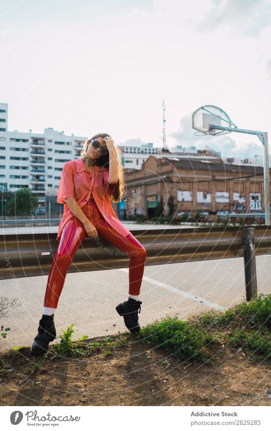 Frau, die auf dem Spielplatz in einem Zaun sitzt. Stil Straße Stadt Körperhaltung Sonnenbrille Porträt attraktiv Beautyfotografie trendy Lifestyle hübsch Mode