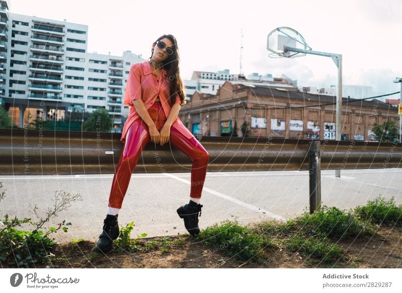 Frau, die auf dem Spielplatz in einem Zaun sitzt. Stil Straße Stadt Körperhaltung Sonnenbrille Porträt attraktiv Beautyfotografie trendy Lifestyle hübsch Mode