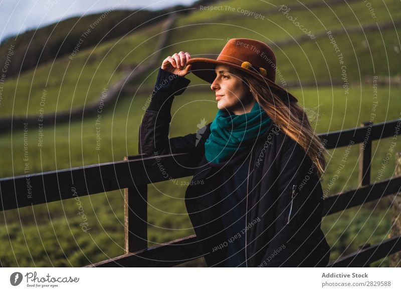 Verträumte Frau, die am Zaun auf dem Feld steht. sitzen grün Natur Wiese stehen träumen Erholung ruhen Wegsehen Hut Frühling Sommer Gras Landschaft