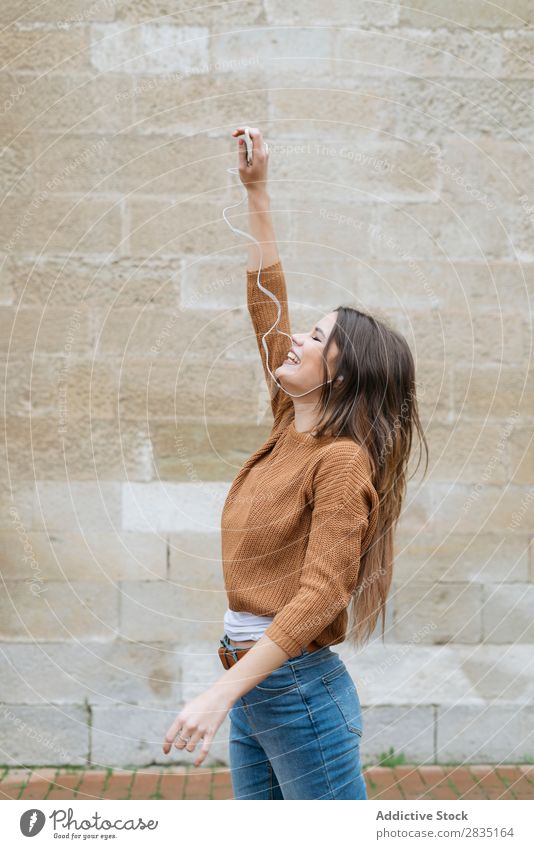 Glückliche Frau mit der Hand in den Kopfhörern hochreichen Lächeln Telefon Backstein Wand Mensch Mobile Internet Technik & Technologie Halt Kaukasier