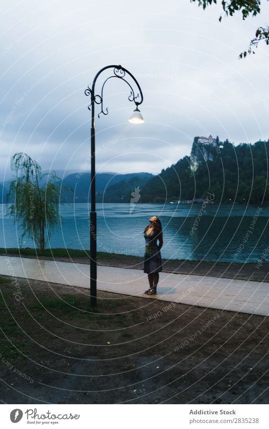 Frau, die auf den Laternenpfahl schaut. laufen See aufschauend Lampe Abend Küste Aussicht Natur Wasser Landschaft Sommer blau grün schön Szene