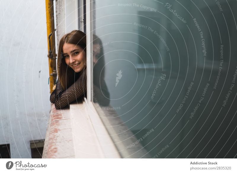 Junges Modell, das im Fenster posiert. Frau Körperhaltung Ausschau haltend Beautyfotografie Zufriedenheit Porträt heiter Straße romantisch träumen Wohnung