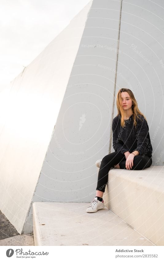 Außenportrait eines jungen Mädchens auf einer Betontreppe mit Blick in die Kamera. Frau Sitzen Klotz Treppe Gebäude verträumt nachdenklich besinnlich