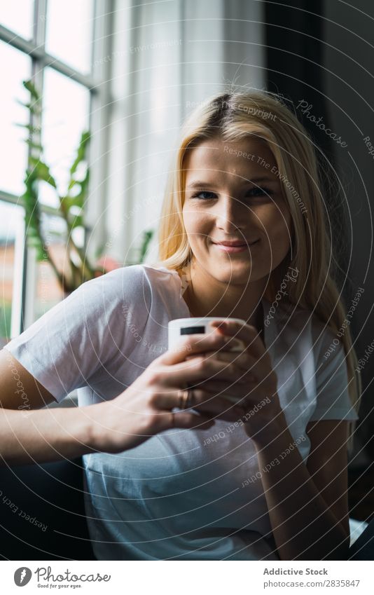 Lächelnde Frau mit Tasse hübsch heimwärts Jugendliche blond erfreut trinken Blick in die Kamera schön Lifestyle Beautyfotografie attraktiv Porträt Dame Raum