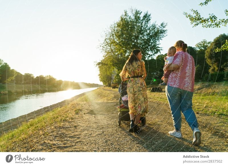 Lesbisches Paar mit Kind im Park Mutter laufen Wagen grün Sonnenstrahlen Glück Mensch Frau Fröhlichkeit Sommer Lifestyle Liebe gleichgeschlechtliche Eltern