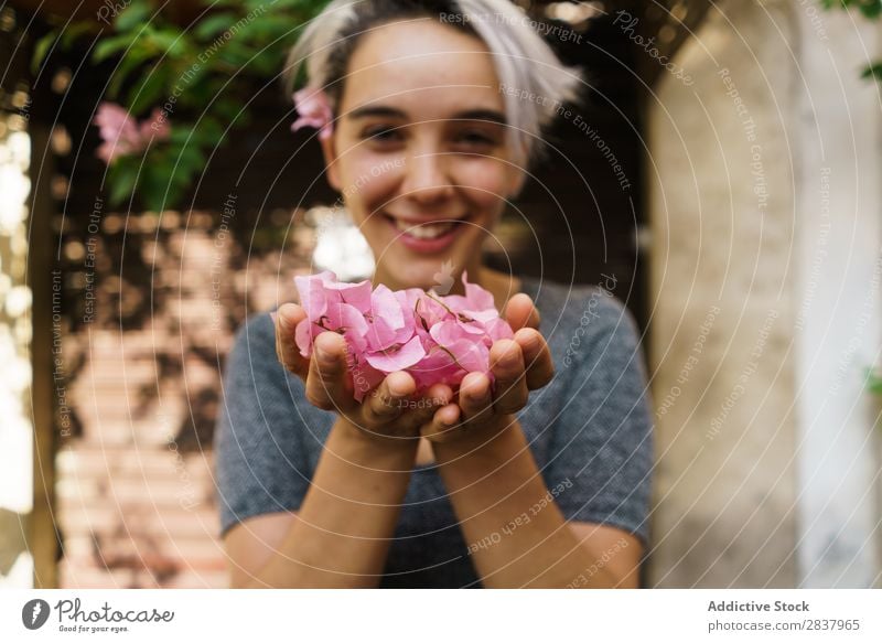 Frau, die Blütenblätter aus den Händen bläst. Blume Straße Blütenblatt wehen Blick in die Kamera schön romantisch Frühling Mädchen Sommer geblümt Sonnenstrahlen