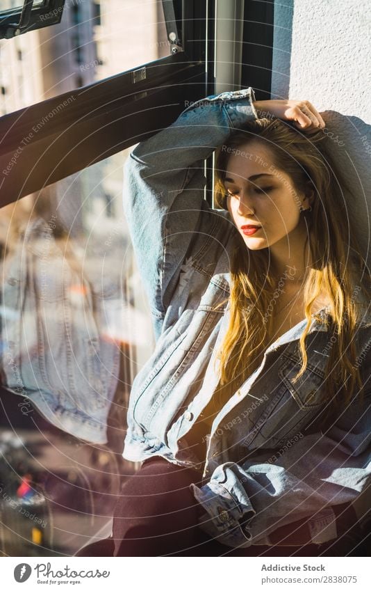 Stylisches Mädchen sitzt am Fenster im Licht. Frau Stil sitzen Körperhaltung Bekleidung Lippen genießen lange Haare Lippenstift träumen Jeansstoff Sonnenlicht