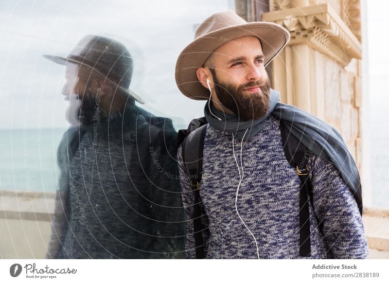 Fröhlicher bärtiger Mann hört Musik. Kopfhörer Stil Blick in die Kamera heiter Zufriedenheit Porträt stehen Jugendliche Lifestyle Hut gutaussehend Typ lässig