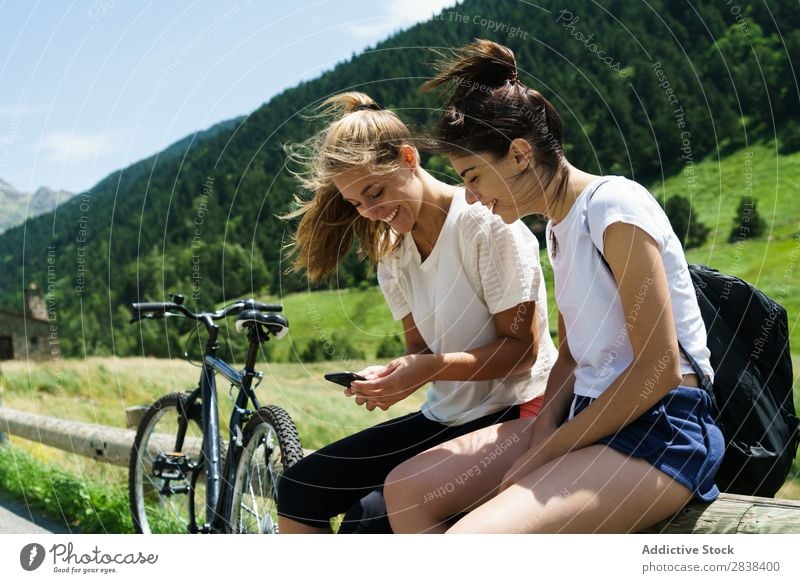 Frauen mit Fahrrädern beim Surfen im Smartphone sitzen Zaun PDA Browsen sportlich Fahrrad Freundschaft Sport Zyklus Mädchen Aktion Lifestyle Fahrradfahren