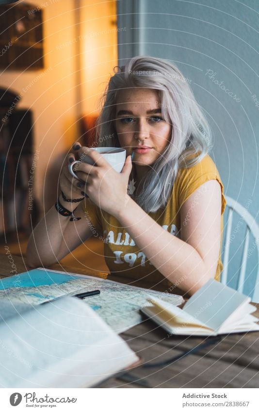 Verträumte Frau mit Tasse hübsch heimwärts Jugendliche blond sitzen Tisch Buch Landkarte Wege & Pfade schön Lifestyle Beautyfotografie Blick in die Kamera