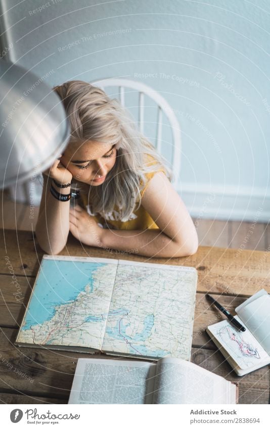 Frau, die sich die Karte im Buch ansieht. hübsch heimwärts Jugendliche blond sitzen Tisch Landkarte Wege & Pfade schön Lifestyle Beautyfotografie attraktiv