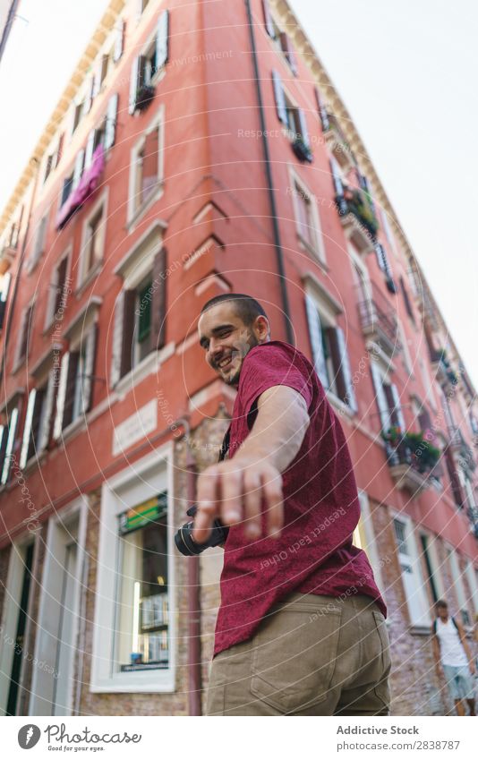 Lächelnder Fotograf, der auf die Kamera zeigt. Mann Stadt Fotoapparat mir folgen heiter Fotografie Sommer Straße Tourist Model auf die Kamera richten