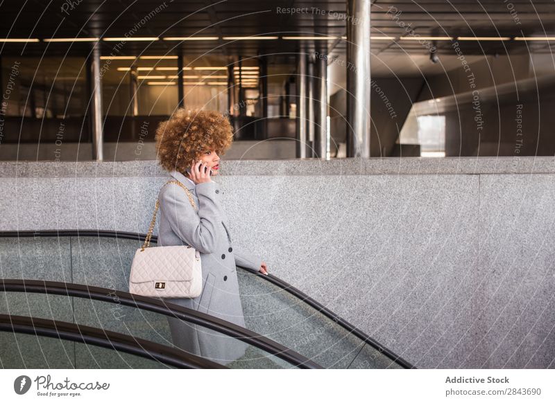 Stilvolle Frau mit Telefon auf der Rolltreppe Erwachsene hübsch PDA sprechen im unteren Stockwerk Haare & Frisuren blond urwüchsig schön attraktiv Mode Model