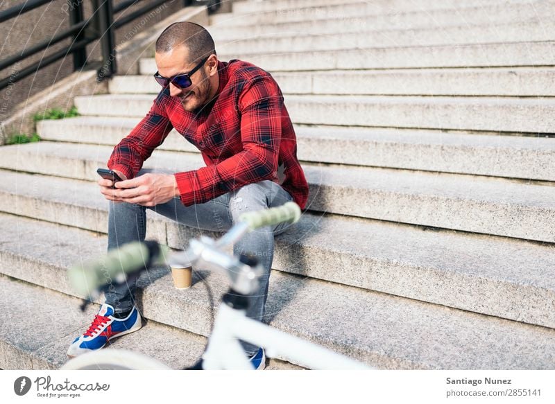 Junger Mann mit Handy und festem Fahrrad. Mobile Fixie Telefon Schickimicki Lifestyle stehen Fahrradfahren Großstadt Gebäude Solarzelle Stadt Mensch