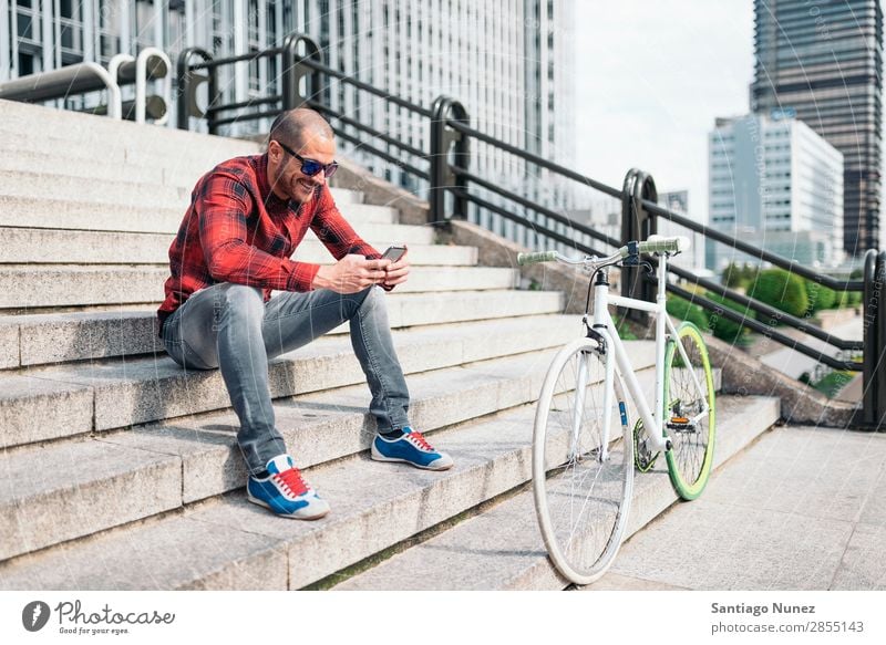 Junger Mann mit Handy und festem Fahrrad. Mobile Fixie Telefon Schickimicki Lifestyle stehen Fahrradfahren Großstadt Gebäude Solarzelle Stadt Mensch