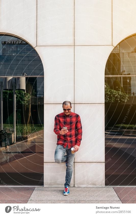 Junger Mann benutzt sein Handy auf der Straße. Mobile Porträt Glück Lächeln Telefon Schickimicki Lifestyle stehen benutzend Großstadt Solarzelle Stadt Mensch