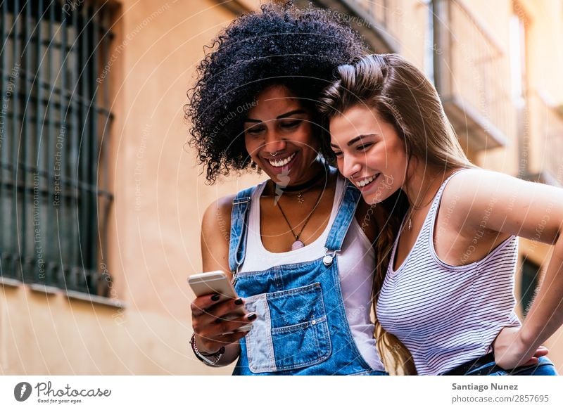 Schöne Frauen, die ein Handy auf der Straße benutzen. Freundschaft Jugendliche Glück Sommer Mensch Freude Mobile PDA Telefon Solarzelle benutzend Mitteilung