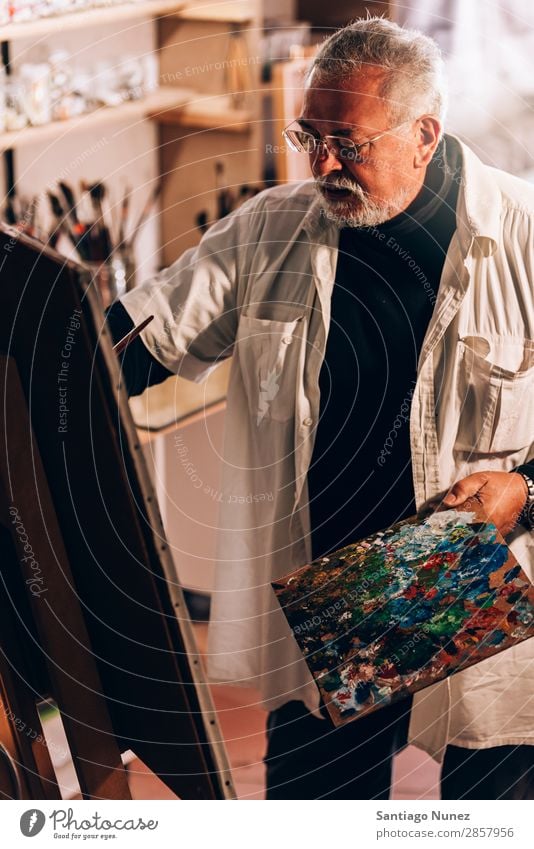 Alter Mann Künstler beim Malen von Ölen in seinem Atelier. Erwachsene Vollbart Maler konzentriert Gemälde Pinsel Bürste Staffelei Leinwand Konzentration