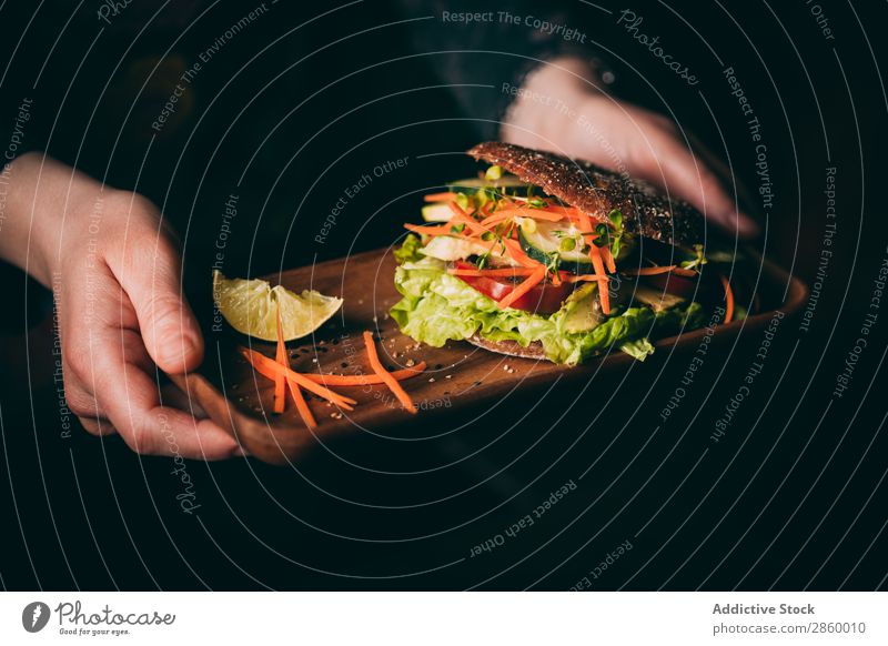 Frau hält ein Tablett mit einem vegetarischen Sandwich. Avocado Biografie Brot Brötchen Burger Möhre Gurke lecker deluxe Diät Öko ökologisch Lebensmittel frisch