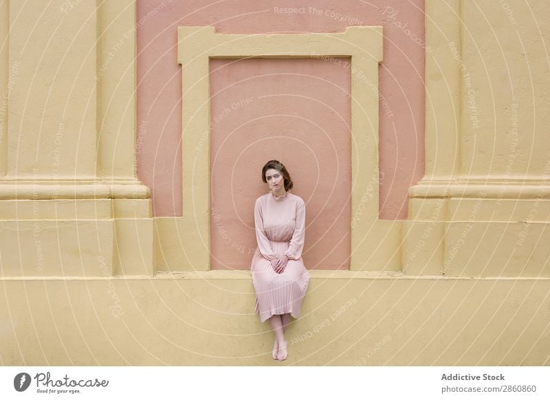 Frau in rosa Kleid, die an der Wand posiert. hübsch Jugendliche altehrwürdig Körperhaltung sitzen schön attraktiv Mensch Beautyfotografie Erwachsene Stil