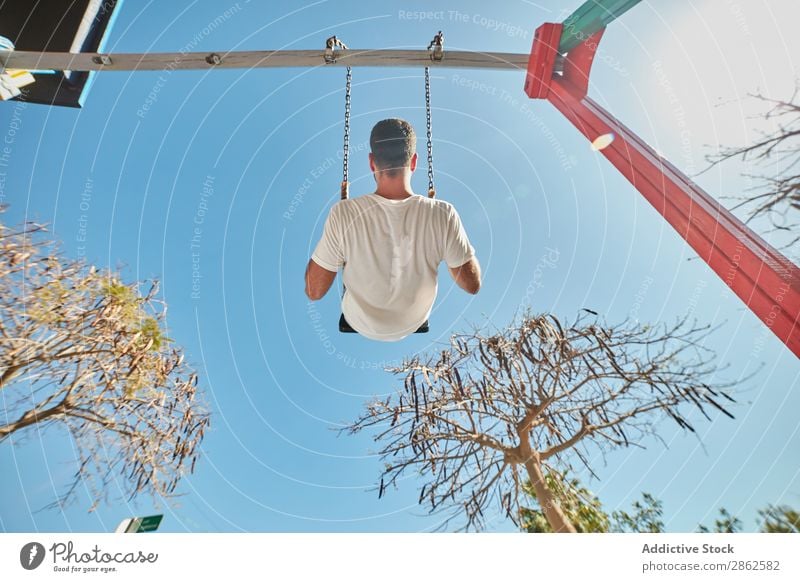 Mann schwingt auf dem Spielplatz bei Sonnenlicht Schaukeln Freizeit & Hobby Stadt hell Blauer Himmel Zufriedenheit Straße Aktion Ausdruck Spielen