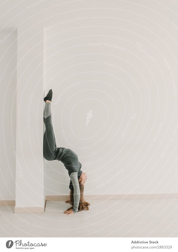 Flexibles Damen-Training auf dem Kopf stehend im Studio Frau beweglich Handstand Beinteilung Seite sportlich Studioaufnahme Licht Raum Fitness üben strecken