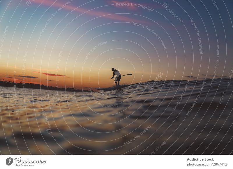 Mann mit Paddel auf dem Surfbrett zwischen Wellenwasser bei Sonnenuntergang Wasser Oberfläche Sport Bali Indonesien Silhouette Himmel Meer Himmel (Jenseits)