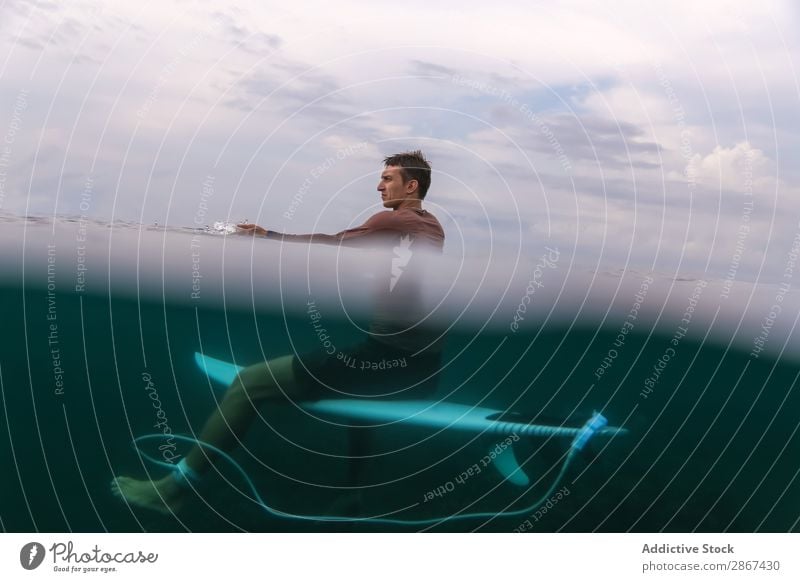 Mann sitzt auf dem Surfbrett und schwimmt im blauen Wasser. Sport Bali Indonesien Surfen winken fliegend Meer Oberfläche sitzen azurblau Rippeln Landschaft