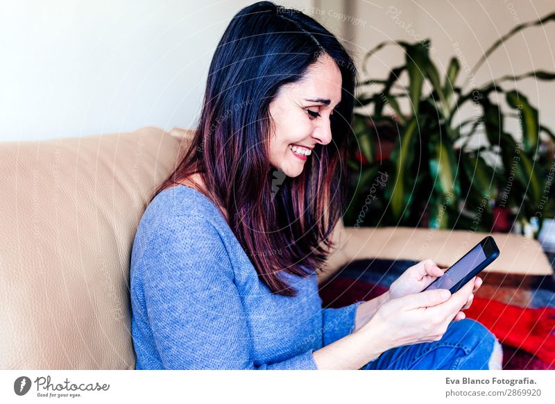 junge Frau, die zu Hause auf dem Sofa sitzt und mit dem Handy telefoniert. Lifestyle Design Arbeit & Erwerbstätigkeit Arbeitsplatz Büro Kapitalwirtschaft