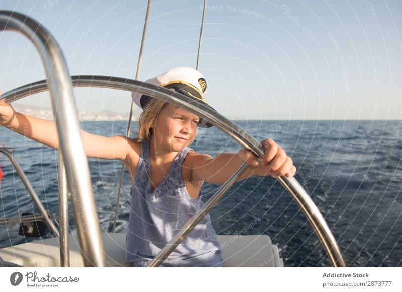 Lächelndes Mädchen hält das Lenkrad auf der Yacht auf dem Wasser. Jacht Kapitän Hut Meer Kind fliegend Schönes Wetter Wasserfahrzeug teuer aussruhen positiv