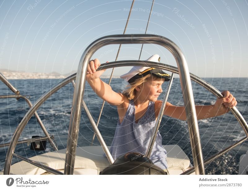 Lächelndes Mädchen hält das Lenkrad auf der Yacht auf dem Wasser. Jacht Kapitän Hut Meer Kind fliegend Schönes Wetter Wasserfahrzeug teuer aussruhen positiv