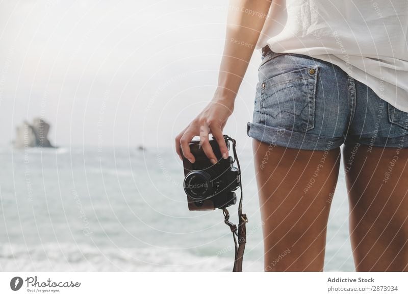 Dame mit Kamera an Land in der Nähe von Steinen und Wasser Frau Fotokamera Küste Meer Jugendliche Lifestyle laufen Felsen natürlich charmant Gerät Apparatur