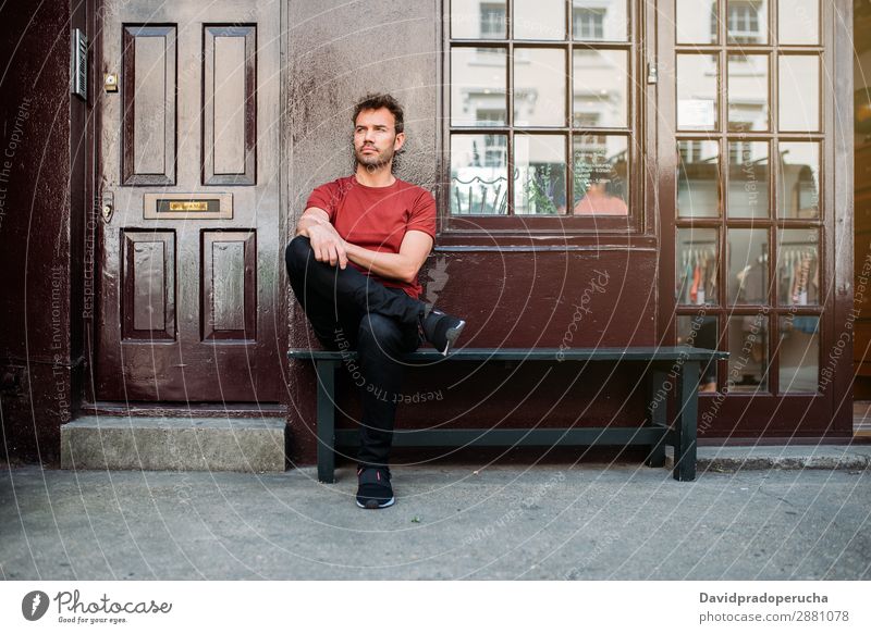 Mann sitzt auf einer Bank auf einem schönen kastanienbraunen Hintergrund. Kaukasier Gebäude Jugendliche Architektur altehrwürdig Nottinghill Dekor Straße sitzen