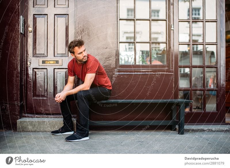 Mann sitzt auf einer Bank auf einem schönen kastanienbraunen Hintergrund. Kaukasier Gebäude Jugendliche Architektur altehrwürdig Nottinghill Dekor Straße sitzen