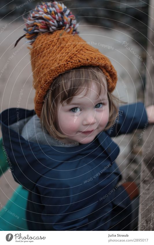 Mädchen mit Strickmütze spielt im Sand feminin Kleinkind 1 Mensch 1-3 Jahre Erde Frühling Winter schlechtes Wetter Garten Regenjacke Mütze brünett kurzhaarig