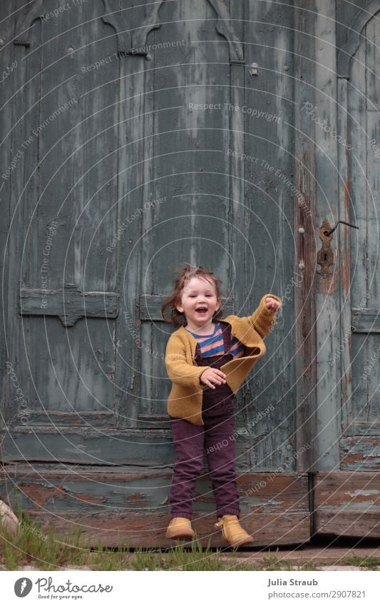 Tor Mädchen hüpfen feminin Kleinkind 1 Mensch 1-3 Jahre Tür Latzhose Strickjacke brünett kurzhaarig Pony Dutt Bewegung lachen springen frech frei Fröhlichkeit