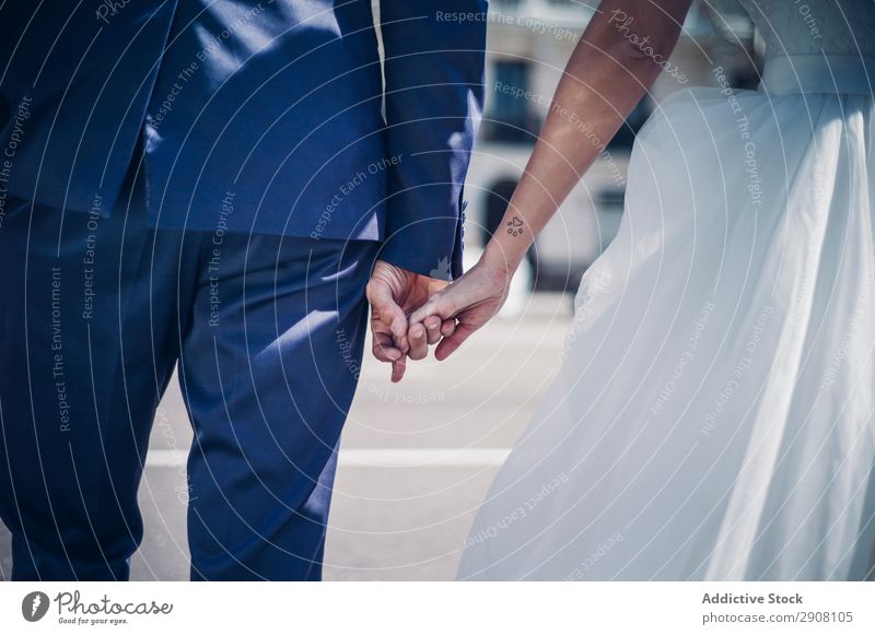 Gerte Mann hält an Händen Frau in Brautkleid auf der Straße an sonnigen Tagen frisch verheiratet Gebäude altehrwürdig elegant Paar Hochzeit Kleid Fenster