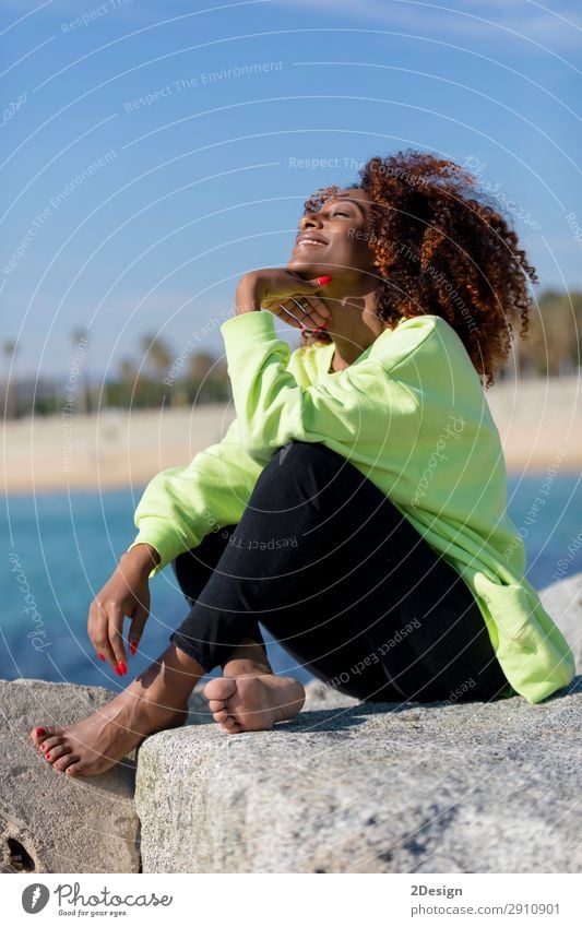 Seitenansicht der schönen lockigen Afrofrau, die auf dem Wellenbrecher sitzt. Lifestyle Stil Haare & Frisuren Gesicht Meer Mensch feminin Junge Frau Jugendliche