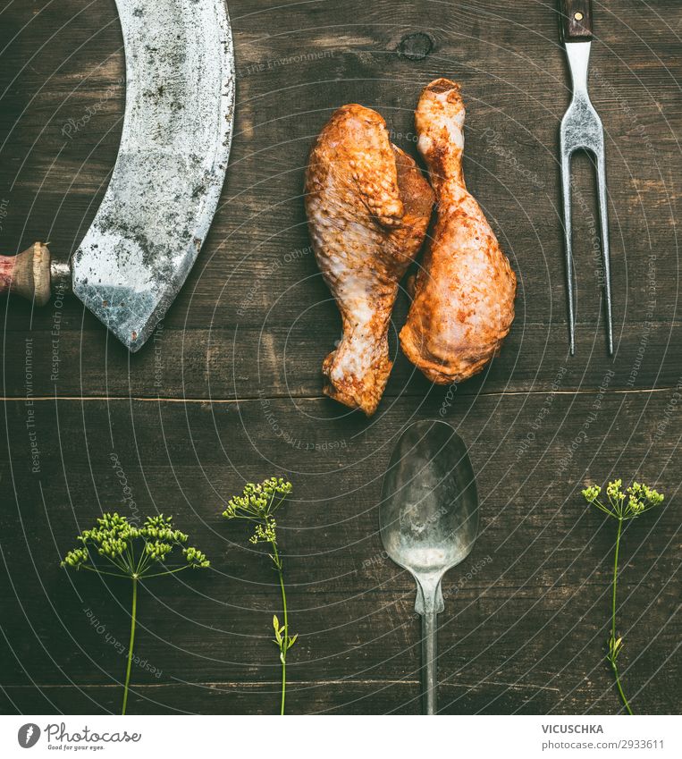 Rohe, vom Grill marinierte Hühnerkeule mit frischen Kräutern und Küchenutensilien auf rustikalem Holzgrund, Draufsicht. Vorbereitung des Grills roh Barbecue