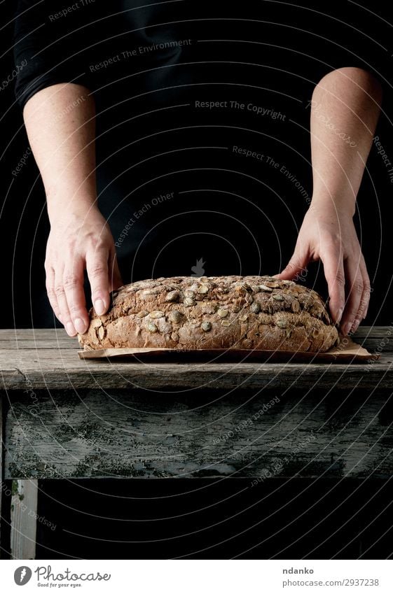 Frauenhände halten ovales, gebackenes Roggenbrot. Teigwaren Backwaren Brot Brötchen Ernährung Essen Frühstück Tisch Küche Erwachsene Hand Wärme Holz machen