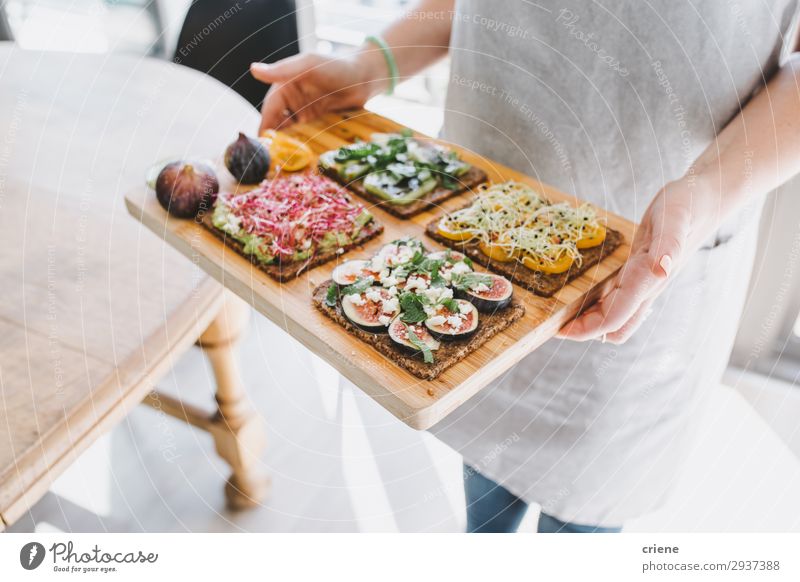 Frau, die ein Holzbrett mit gesunden Sandwiches trägt. Käse Frucht Brot Frühstück Mittagessen Hand Freude Zuprosten Belegtes Brot Gesundheit Küchenkräuter Feige