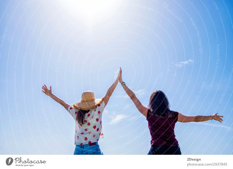 Zwei junge Frauen sitzen auf einem Zaun, die Arme sind gegen den blauen Himmel erhoben. Lifestyle Freude Glück schön Erholung Freizeit & Hobby