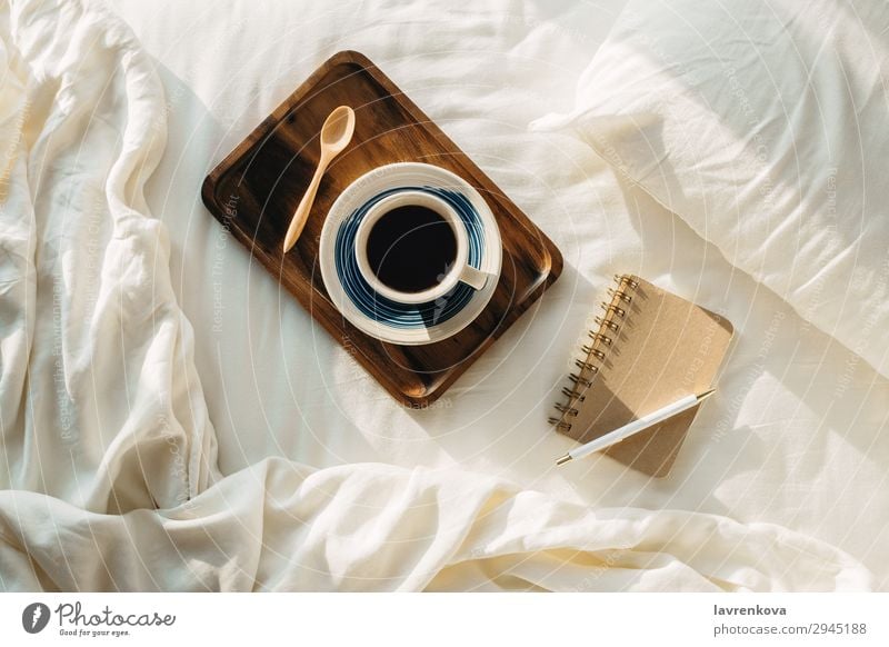 Kaffee auf Holztablett mit Notizbuch und Stift auf dem Bett Flachlegung Tablett Löffel Tee Schlafzimmer Laken Kopfkissen Schreibstift heiß Papier Tasse Becher