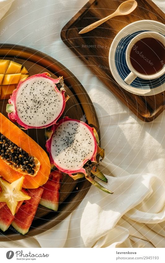 Kaffee oder Tee auf Holztablett und tropischem Obstteller exotisch Karambole Mango Pitahaya Drachenfrucht Teller Gesunde Ernährung Pflanzenbasiert